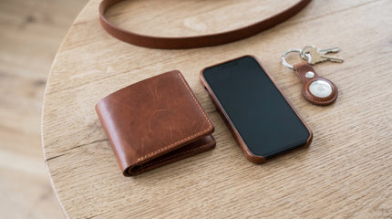 Markore Assam Silk bifold wallet and Markore Tag Mate keychain and Shell Guard iphone case sitting on a table with Gul Sahar crossbody bag strap visible.