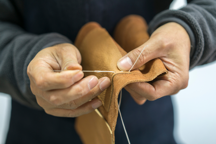 Artisan crafting a brown leather wallet with a needle and thread sewing saddle stitches