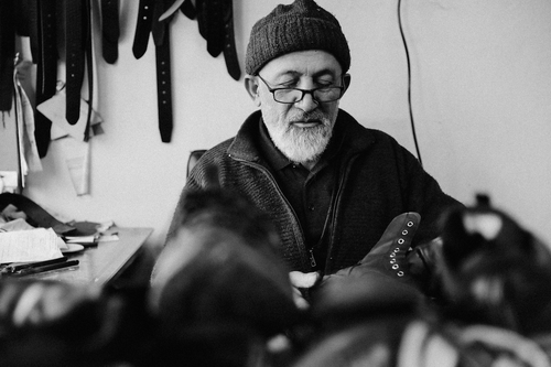 Black and white photo of an artisan working with shoes in a leather workshop.