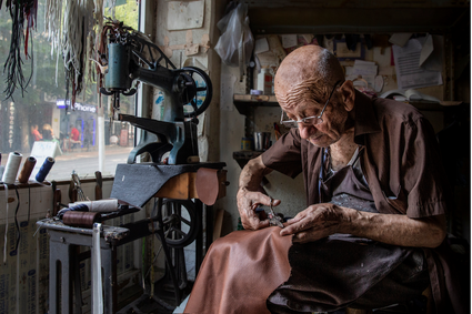 Artisan sitting next to a sewing machine in a workshop cutting leather