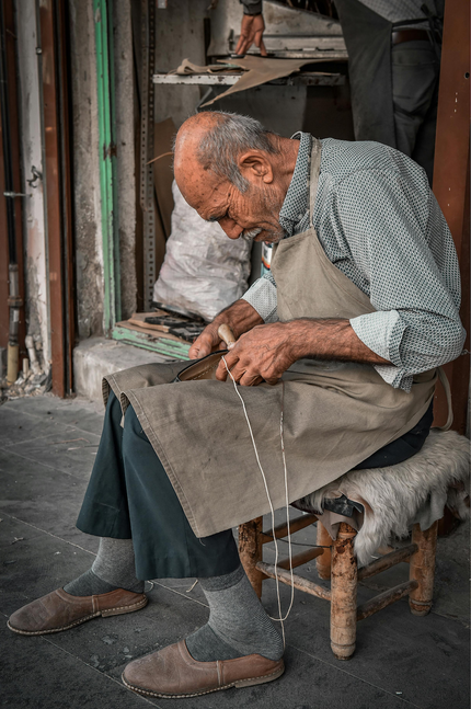Artisan sitting on a stool in front of a workshop crafting leather goods