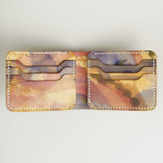 Unfolded inside view of hand-painted full-grain bifold leather wallet in purple, amber, and brown, featuring handmade stitching. Markore Canvas Chaos.