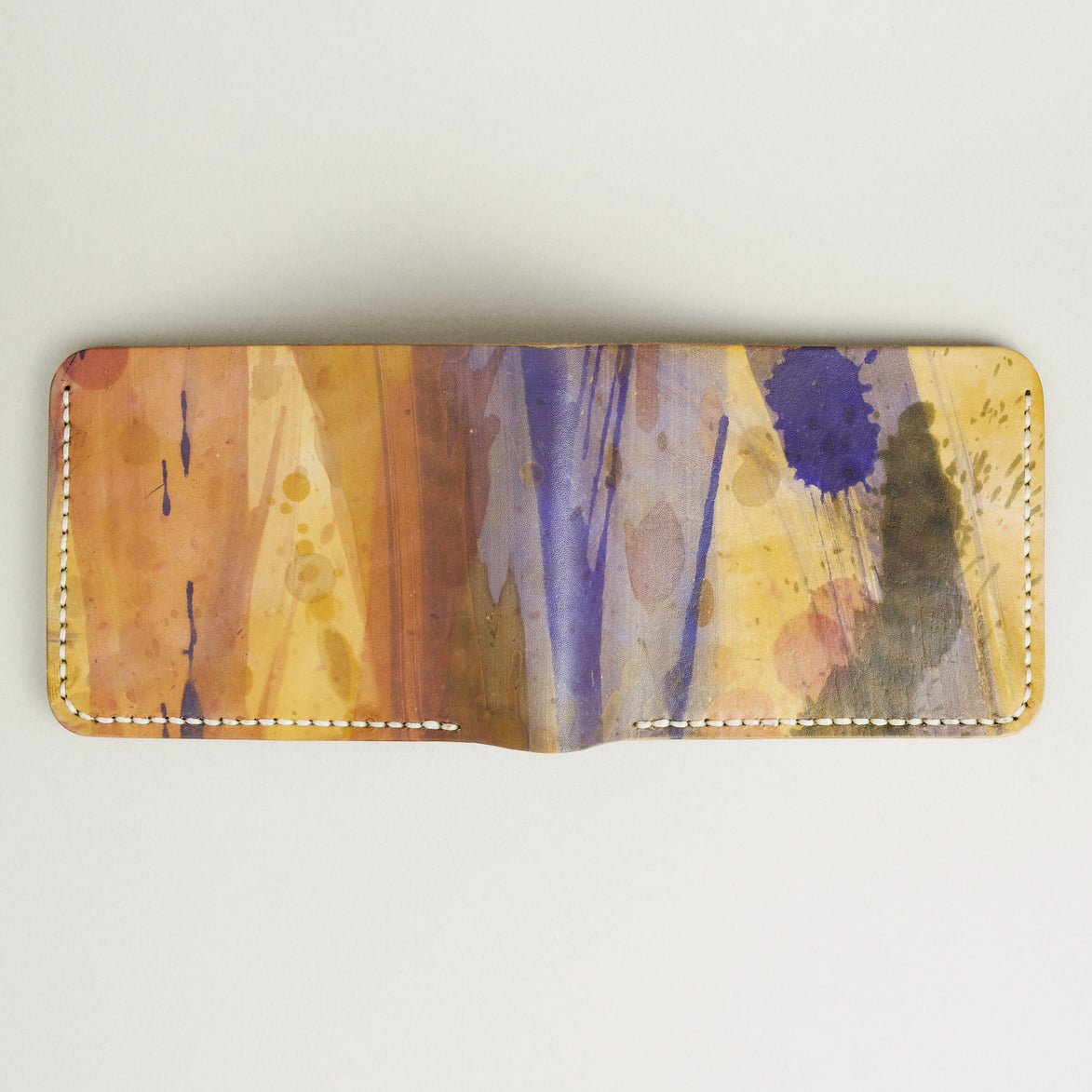 Unfolded outside view of hand-painted full-grain leather bifold wallet in purple, amber, and brown, featuring handmade stitching. Markore Canvas Chaos.