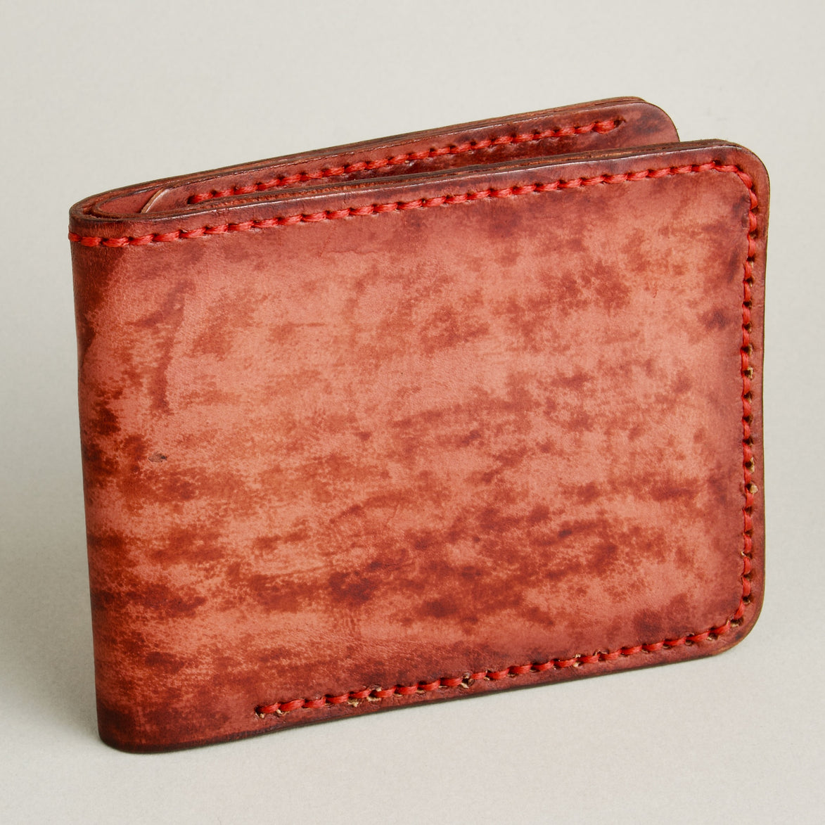 Side view of hand-painted full-grain leather bifold wallet in red, featuring handmade stitching. Markore Canvas Flame.