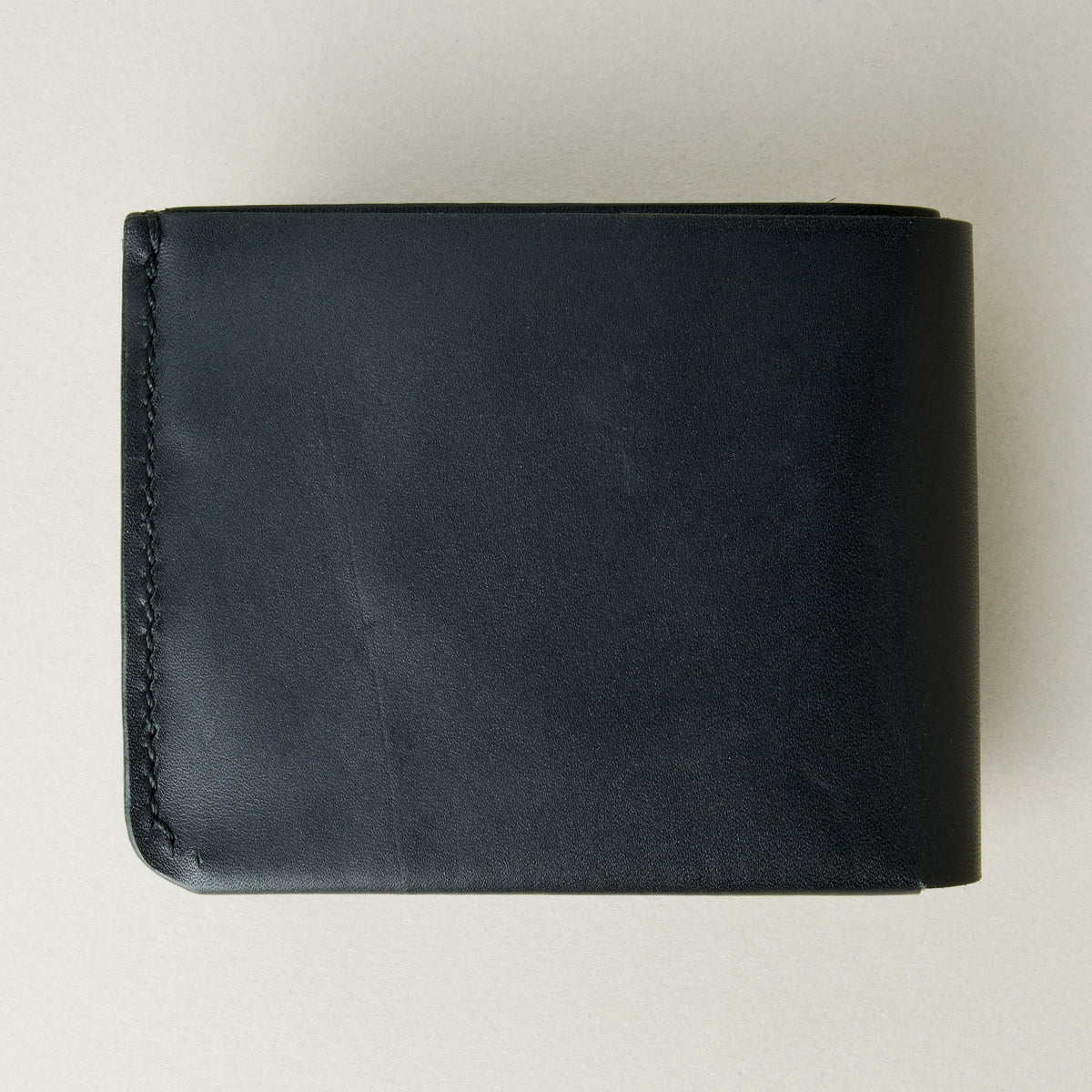 Back view of midnight black full-grain leather wallet featuring a seamless bottom edge and handmade stitching. Markore Assam Silk.
