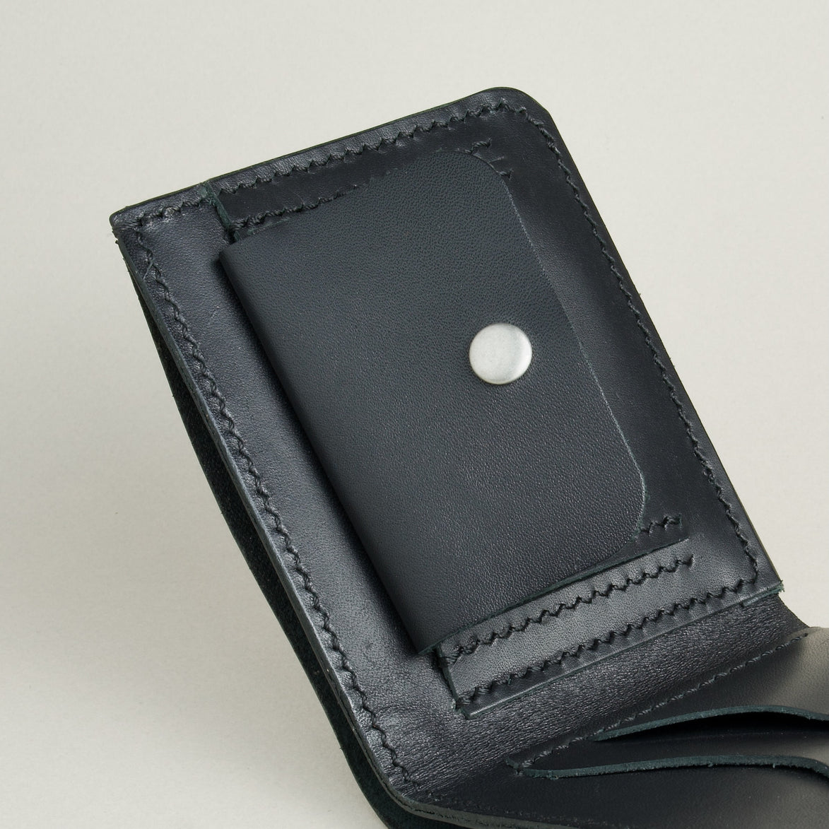 Close up of midnight black full-grain leather wallet featuring a coin pocket with stainless steel press stud and handmade stitching. Markore Assam Silk.
