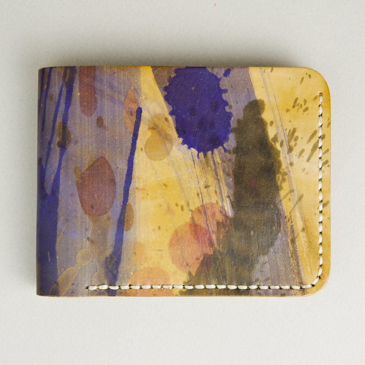 Front view of hand-painted full-grain leather bifold wallet in purple, amber, and brown, featuring handmade stitching. Markore Canvas Chaos.