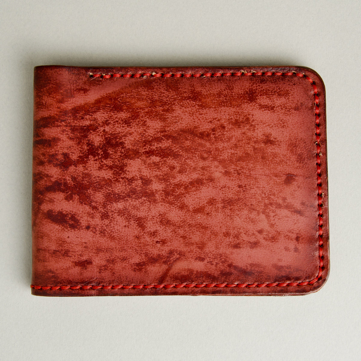 Front view of hand-painted full-grain leather bifold wallet in red, featuring handmade stitching. Markore Canvas Flame.