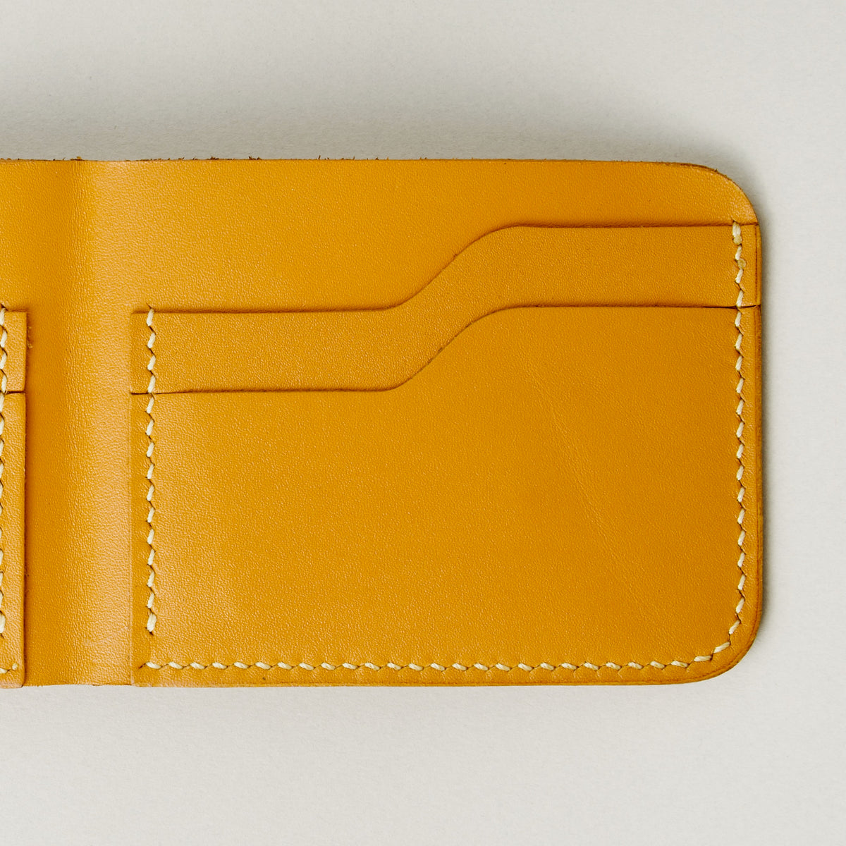 Detail of full grain leather bifold wallet in amber, featuring ivory handmade stitching card slots. Markore Hunza Fold.