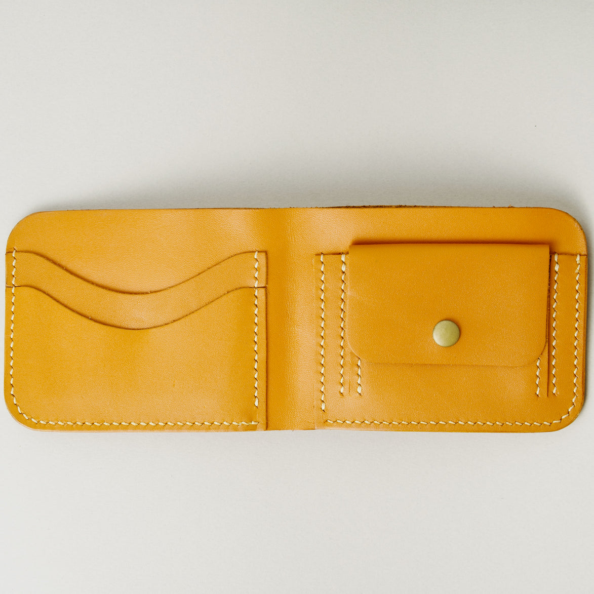 Inside view of full grain leather bifold wallet in amber, featuring ivory handmade stitching, a coin pocket with brass press stud and card slots. Markore Hunza Fold.