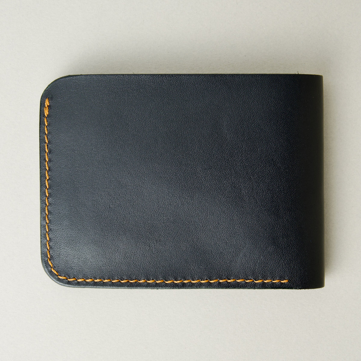 Back view of full grain leather bifold wallet in midnight black, featuring handmade stitching in amber. Markore Hunza Fold.