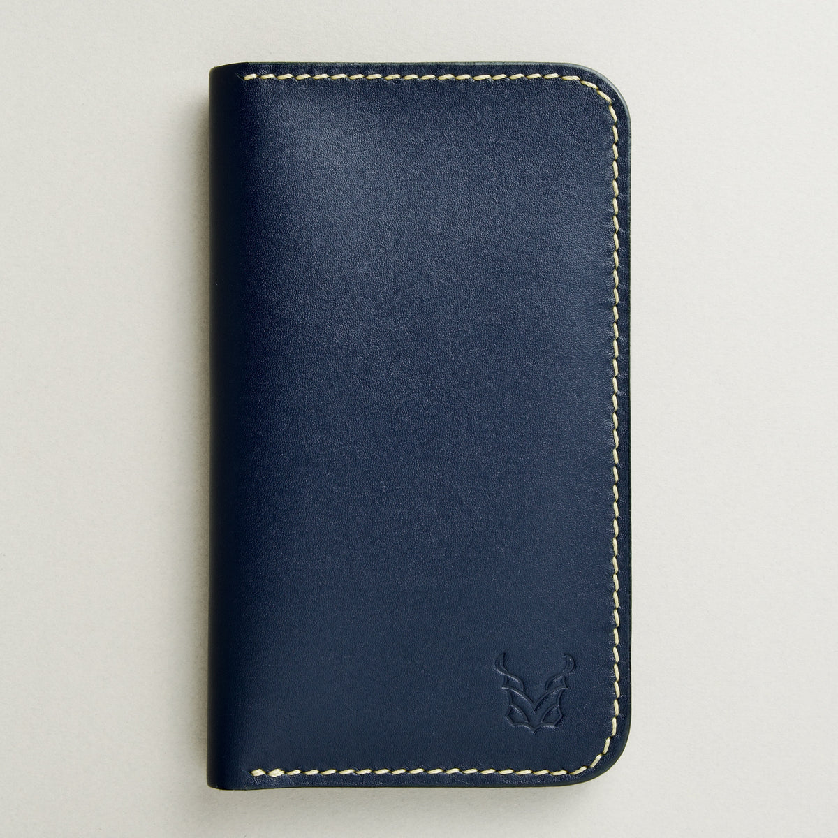 front view of vertical full-grain leather bifold wallet in dark blue, featuring handmade stitching in ivory and embossed logo. Markore Karakoram II.