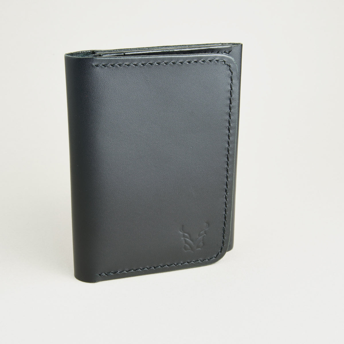 Outside view of midnight black full-grain leather flap fold wallet featuring a flap closure, handmade stitching and embossed logo. Markore Khaas Andaz.
