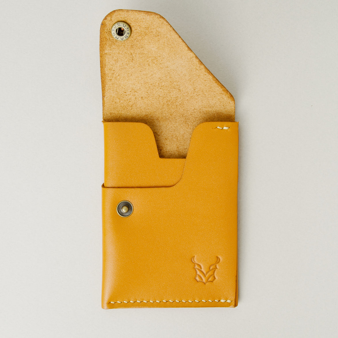 Front view of full grain leather card in amber with ivory handmade stitching, featuring an open flap with brass press button, card slots and embossed logo. Markore Niva Heritage.