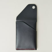 Back view of full grain leather card holder in black with red handmade stitching, with an open flap with stainless steel press button and embossed logo. Markore Niva Heritage.