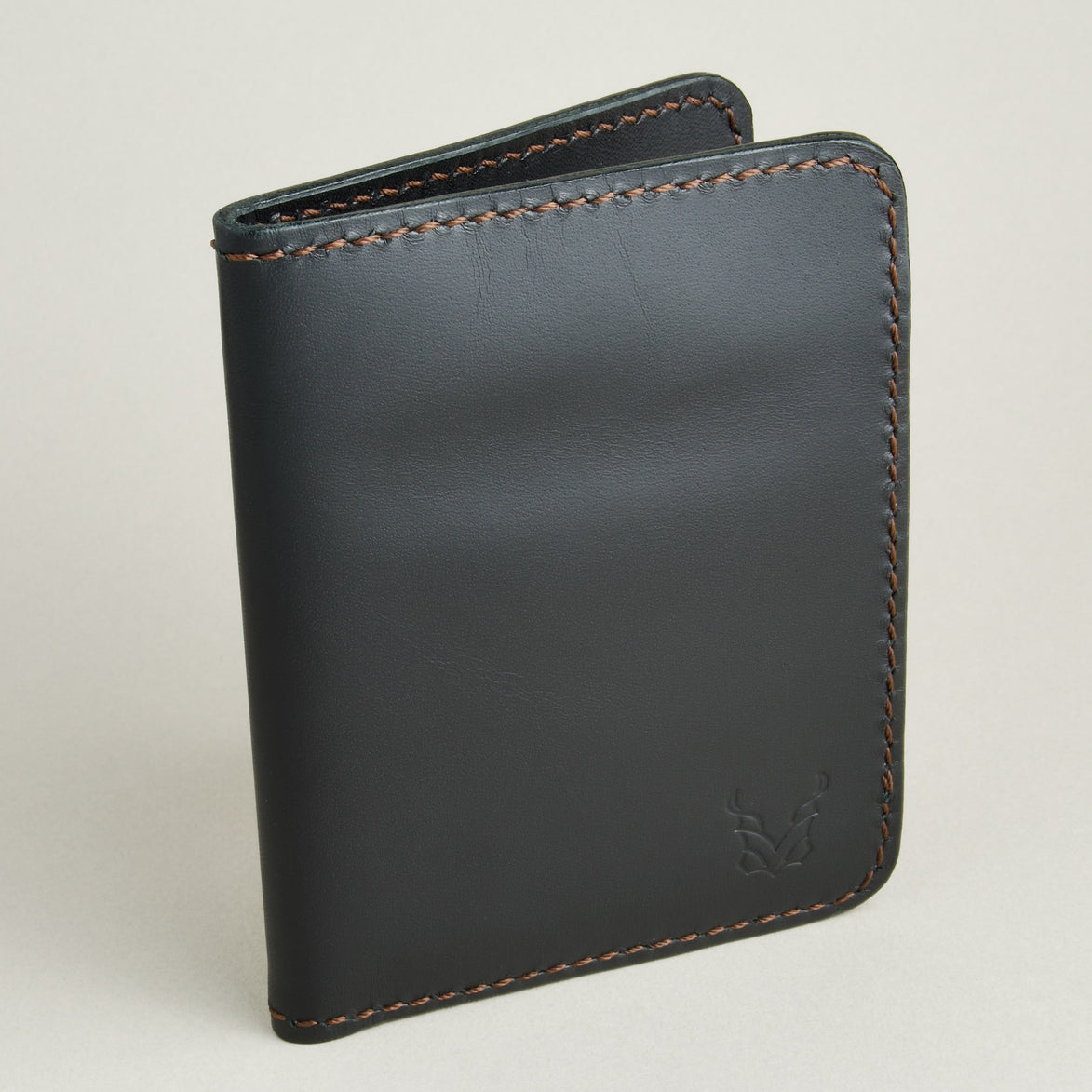 Side view of midnight black full-grain leather wallet featuring espresso brown handmade stitching and embossed logo. Markore Ravi Fold.