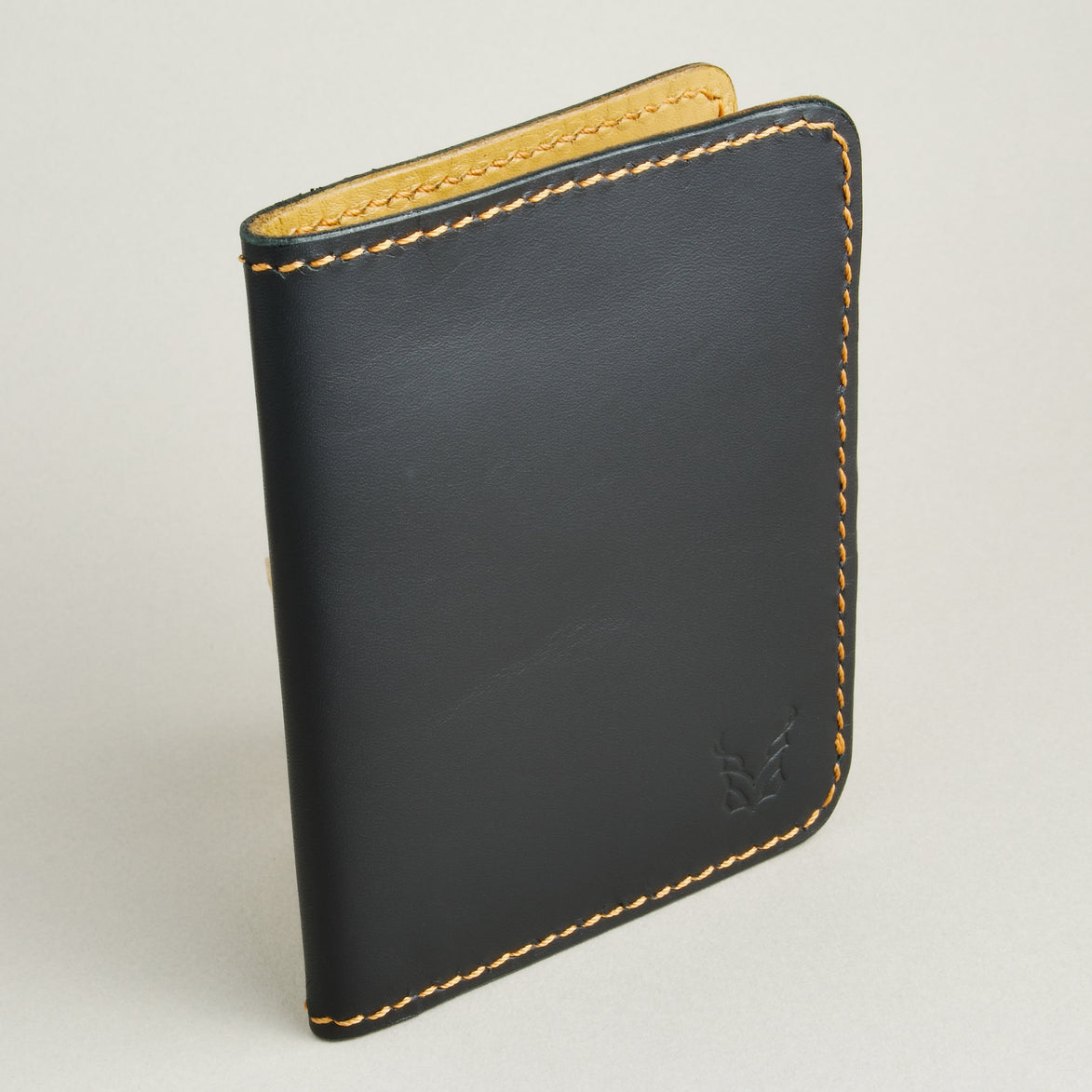 Side view of midnight black full-grain leather wallet featuring amber handmade stitching and embossed logo. Markore Ravi Fold.