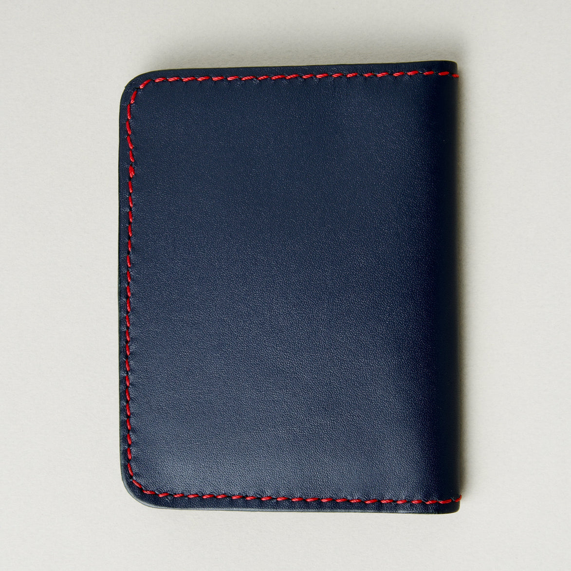 Back view of dark blue full-grain leather wallet featuring red handmade stitching. Markore Ravi Fold.