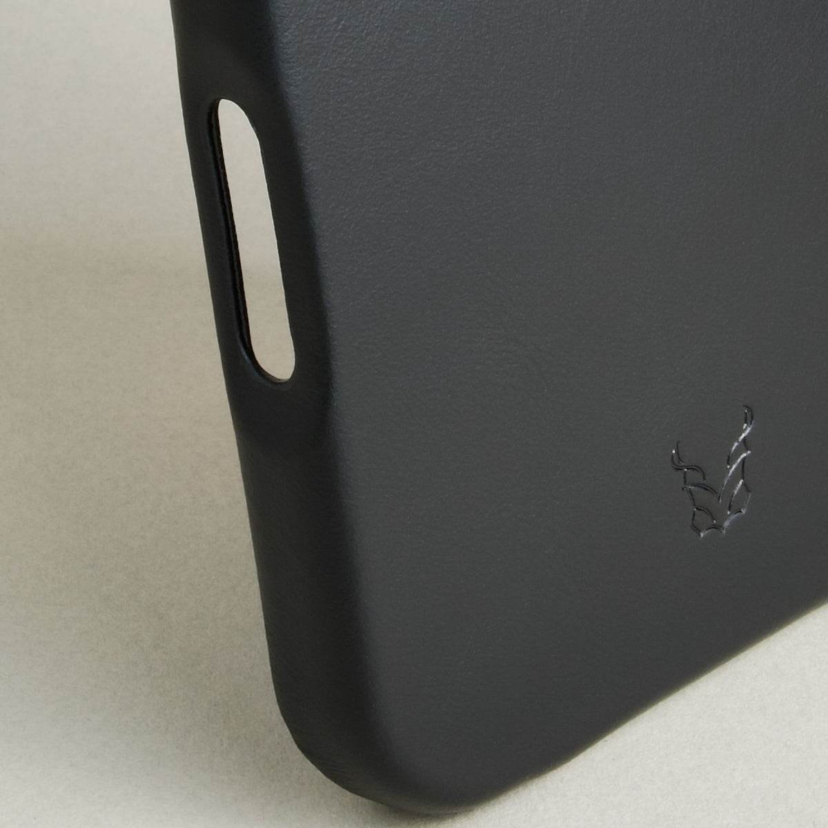 Detail of midnight black leather iphone 17 pro case featuring button cutout and embossed logo. Markore Shell Frame.