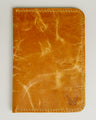 Front view of vertical full-grain leather passport holder in amber, featuring handmade stitching and embossed logo. Markore Voyage Pass.