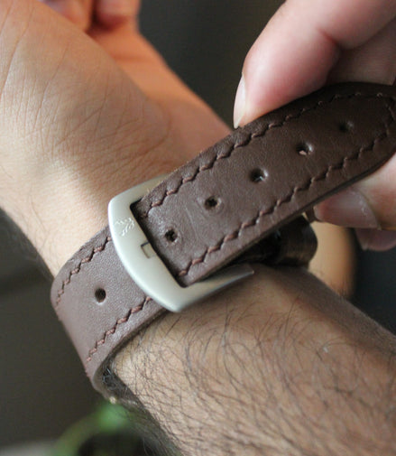 Person adjusting a brown leather markore hour line apple watch strap
