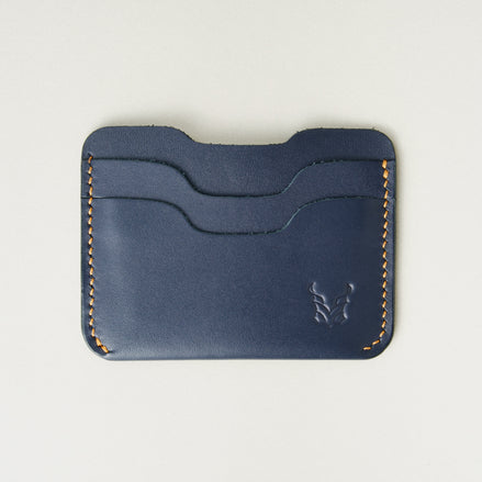 Front view of dark blue full-grain leather card sleeve featuring card slots, amber handmade stitching and embossed logo. Markore Niva Zoj.