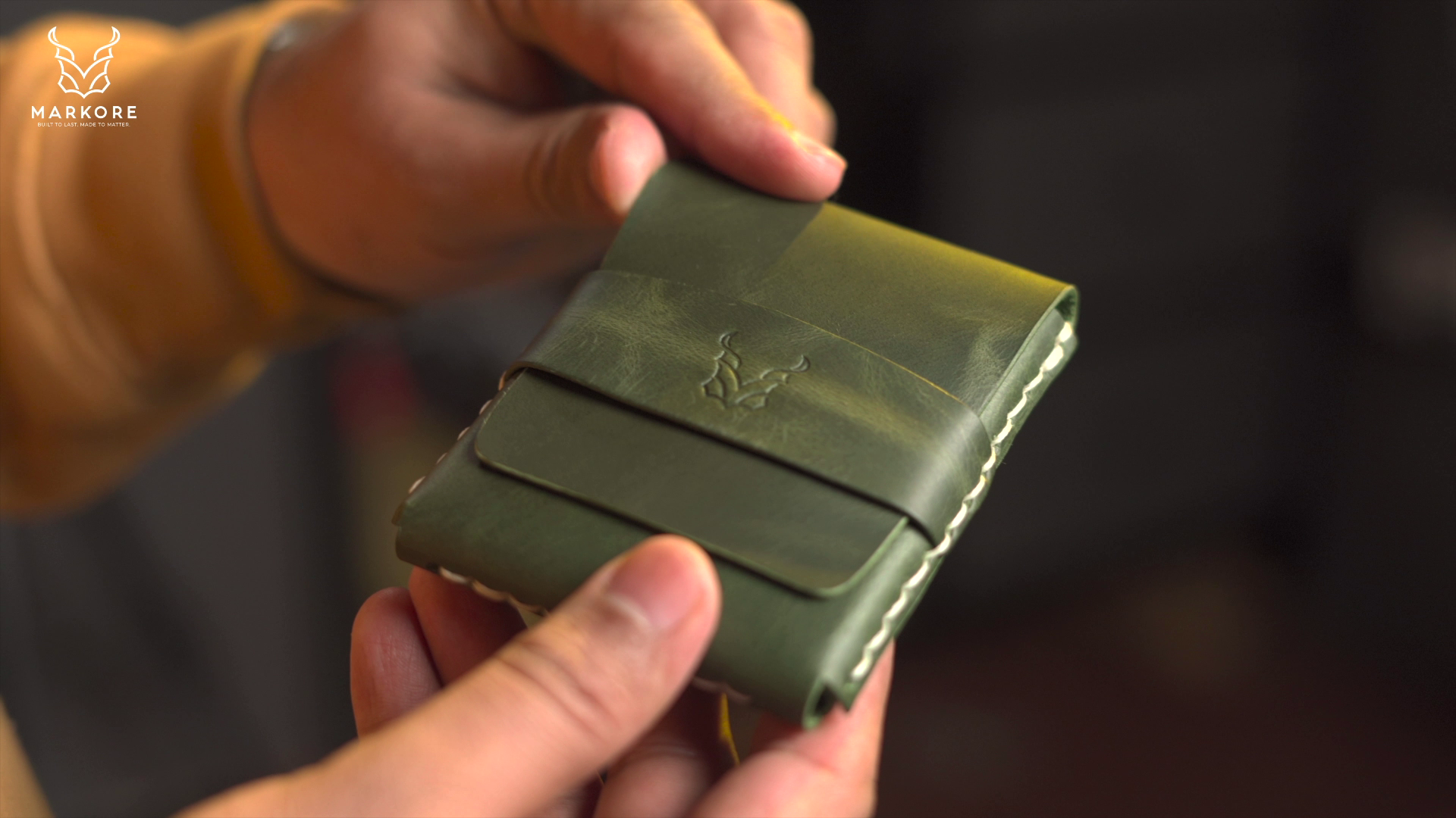 Hand holding a green leather flap wallet with Markore logo