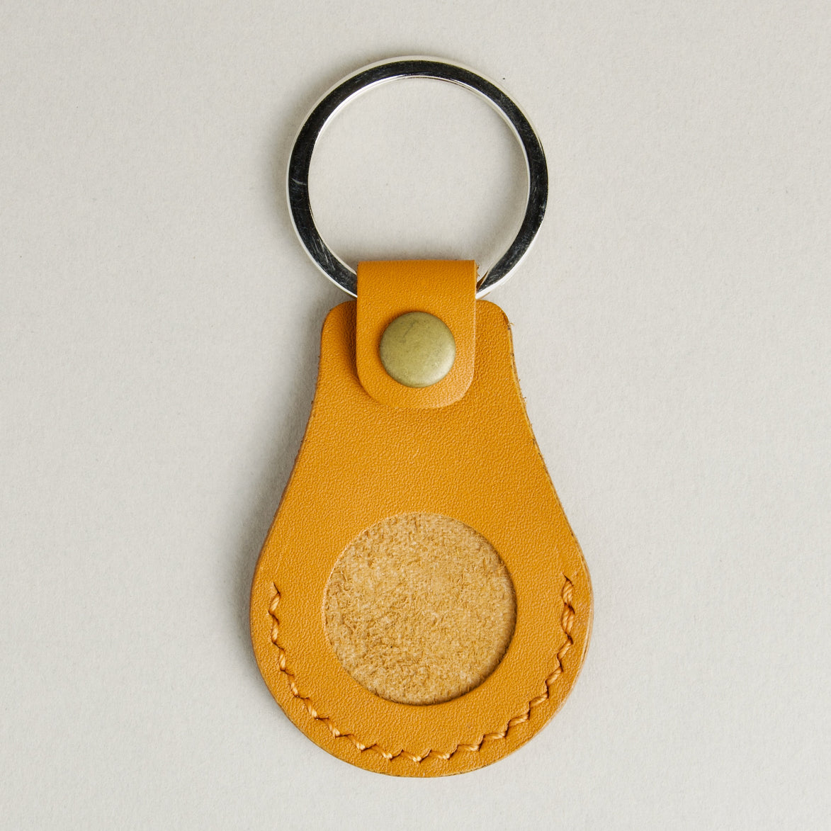 Front view of amber AirTag keychain in full-grain leather with round metal key ring and brass press stud. Markore Tag Mate.
