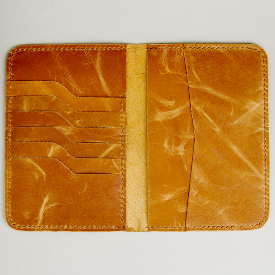 Inside view of vertical full-grain leather passport holder in amber, featuring passport, cash and card slots, and handmade stitching. Markore Voyage Pass.